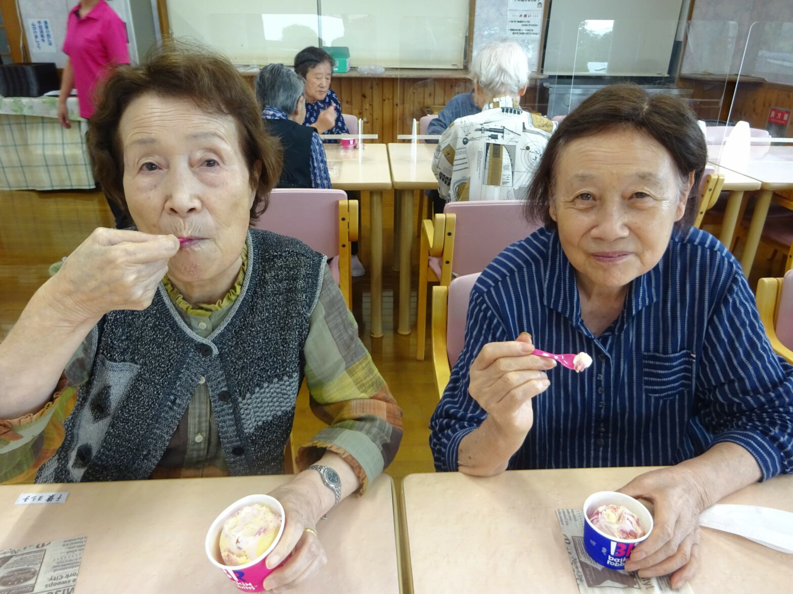 食堂で入居者が食事やおやつを楽しむ風景。複数の高齢者が笑顔で過ごしている。
