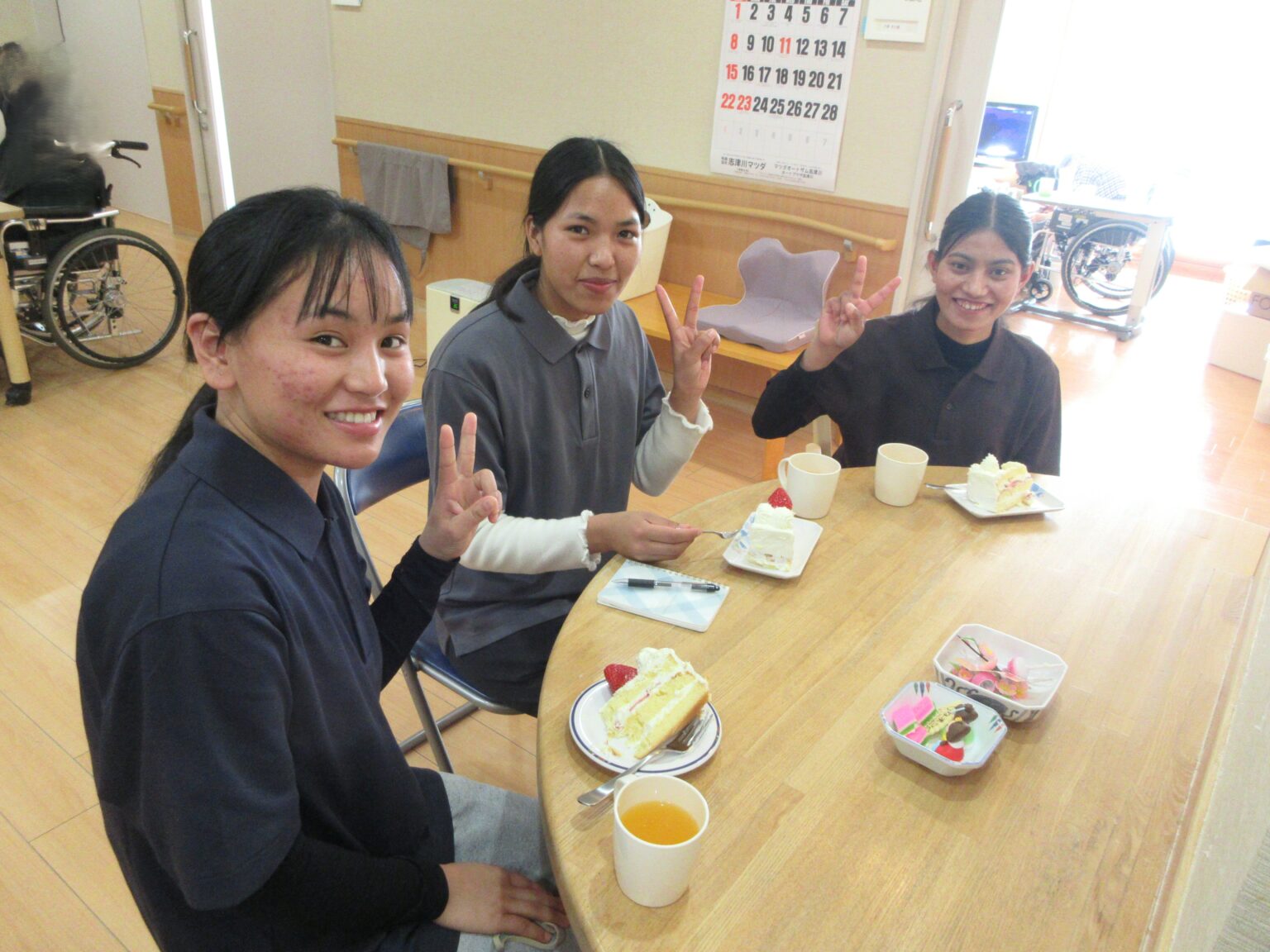 介護施設でのレクリエーション。若い職員や利用者が笑顔で食事やお茶を楽しんでいる風景