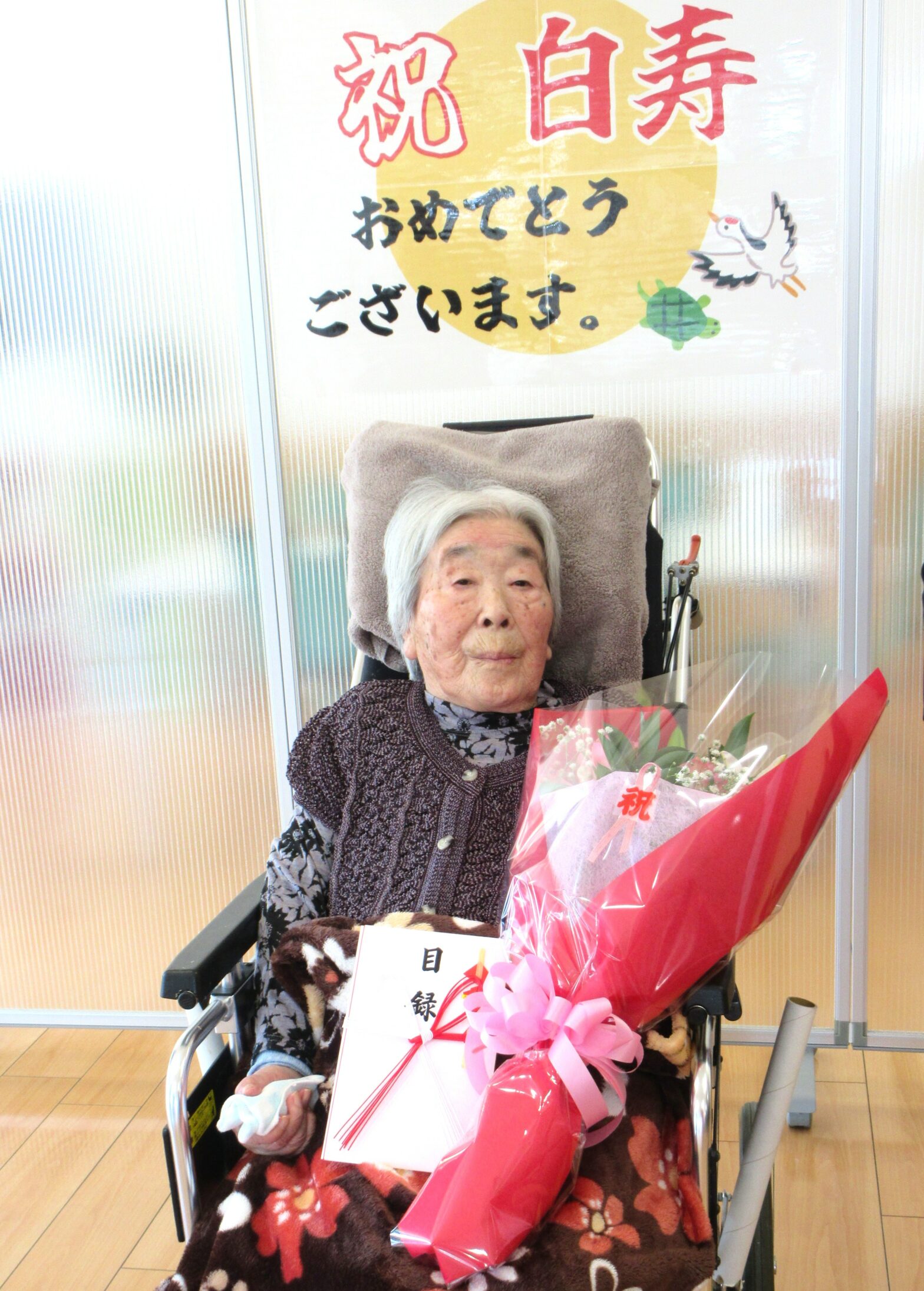 百寿祝いのイベントで、花束を持つ高齢入居者の記念写真